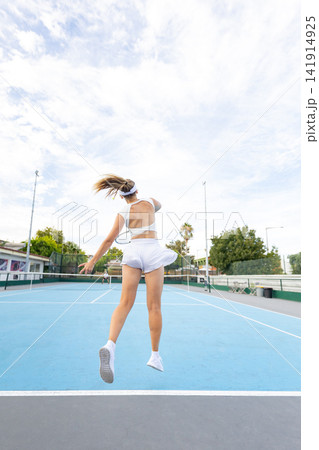 Woman athlete jumping hitting tennis ball during match Woman athlete jumping hitting tennis ball during match 141914925