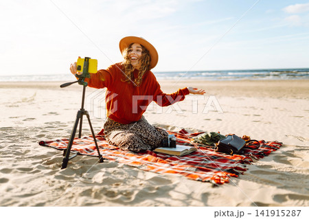 Style woman using smartphone with stabilizer, taking pictures in on sea beach. Woman creates content 141915287