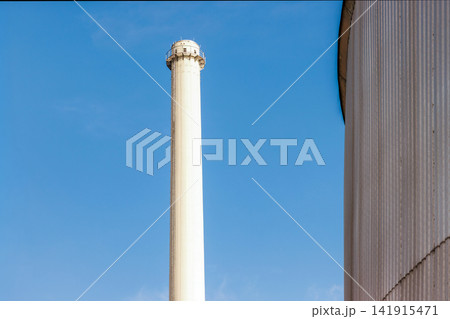 Minimal industrial smokestack and ribbed silo against blue sky. Copy space Minimal industrial smokestack and ribbed silo against blue sky. Copy space 141915471