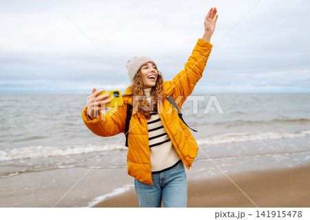 Portrait of young tourist in yellow jacket with phone in hands on seashore. Travel concept, blogging Portrait of young tourist in yellow jacket with phone in hands on seashore. Travel concept, blogging 141915478