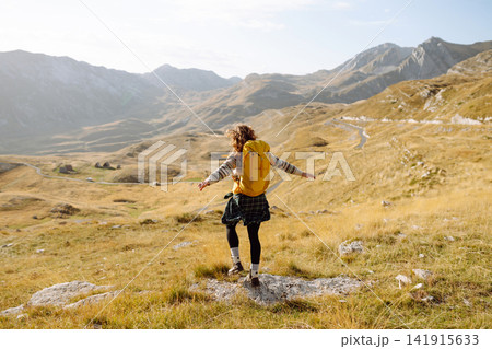 Traveler woman with a bright yellow backpack strolls through golden meadows. Active lifestyle Traveler woman with a bright yellow backpack strolls through golden meadows. Active lifestyle 141915633