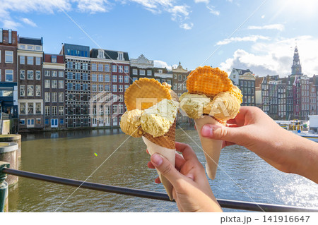 Amsterdam Canal Houses Netherlands. Two Hands Holding Ice Cream Cones with stroopwafel Waffles. Summer street food in travel 141916647