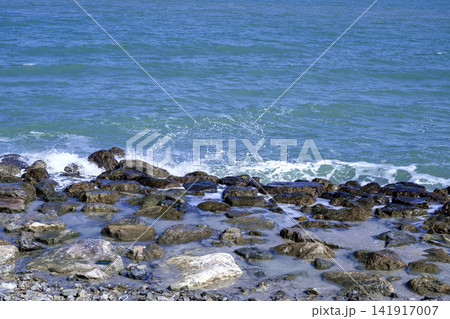 Ocean waves splashing against rocky shore on sunny summer day 141917007