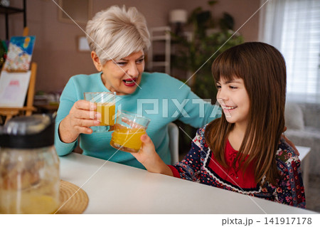 Grandmother and granddaughter sharing orange juice at home 141917178