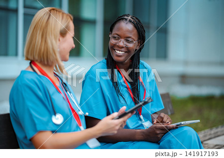 Diverse nurses collaborating outdoors using digital tablets Diverse nurses collaborating outdoors using digital tablets 141917193