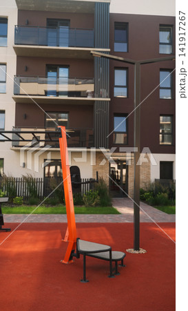 Modern outdoor gym equipment on a red rubber floor in an urban residential area with apartment building Modern outdoor gym equipment on a red rubber floor in an urban residential area with apartment building 141917267