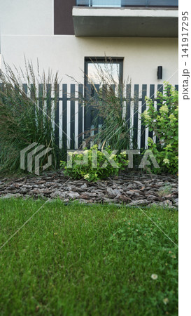 Creating modern landscape design with ornamental grass, shrubs, mulch, and a sleek fence separating lawn from architecture 141917295