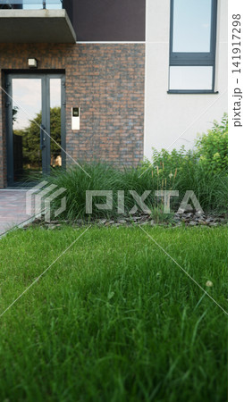 Modern building exterior showcasing green lawn, decorative plants, brick facade, and front entrance reflecting surrounding nature Modern building exterior showcasing green lawn, decorative plants, brick facade, and front entrance reflecting surrounding nature 141917298