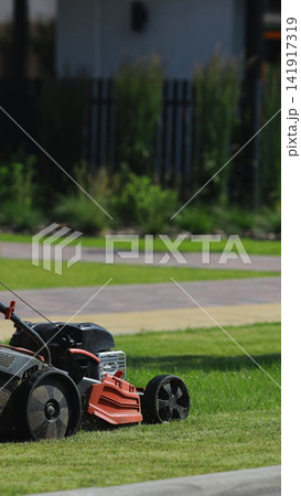 Lawn mower cutting fresh green grass on a sunny day, creating neat turf in a modern home garden 141917319