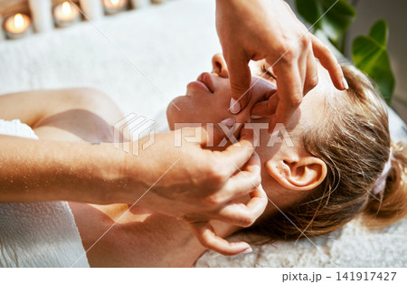 Candlelit Spa Facial Treatment Therapist Fingers Pressing Cheek and Temple of Relaxed Woman on White Towel in Warm Amber Light 141917427