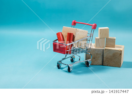 Miniature shopping cart filled with wooden blocks and items next to stacked cubes on a blue background. High Quality Photo 141917447