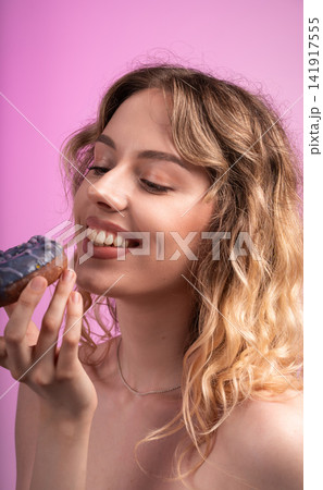 Young woman enjoying sweet donut, face expressive with happiness and dessert craving, pink background Young woman enjoying sweet donut, face expressive with happiness and dessert craving, pink background 141917555