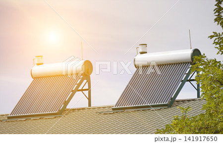 Solar Water Heater Panels with Evacuated Vacuum Tubes Installed on the Roof of a Modern House against Sunrise Sky. Green Ecofriendly Energy System for Residential Infrastructure. 141917650