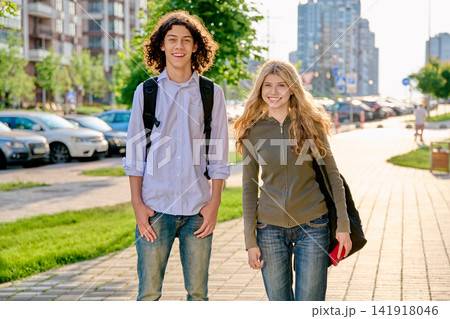 Two happy diverse teenager students with backpacks standing outside on a sunny city street Two happy diverse teenager students with backpacks standing outside on a sunny city street 141918046
