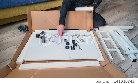 Person assembling flat pack furniture with tools and hardware on wooden floor Person assembling flat pack furniture with tools and hardware on wooden floor 141919843