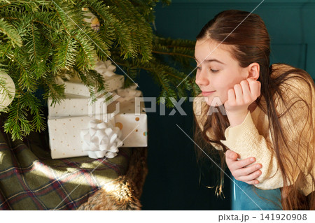 Teen girl relaxing by Christmas tree and wrapped holiday gifts 141920908