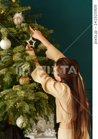 Teen girl decorating Christmas tree with star ornament at home 141920909