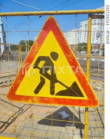 Triangular road work sign with a red border and yellow interior featuring a black silhouette of a person digging with a shovel Triangular road work sign with a red border and yellow interior featuring a black silhouette of a person digging with a shovel 141921162