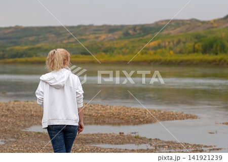 Woman at the river in wilderness is enjoying the autumn view. Woman at the river in wilderness is enjoying the autumn view. 141921239