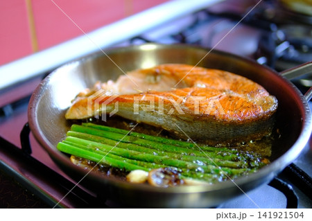 Asparagus frying beside salmon steak with garlic lemon and chili in stainless steel pan with bubbling butter and oil close up healthy seafood cooking Asparagus frying beside salmon steak with garlic lemon and chili in stainless steel pan with bubbling butter and oil close up healthy seafood cooking 141921504