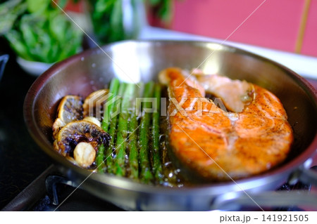 Asparagus frying beside salmon steak with garlic lemon and chili in stainless steel pan with bubbling butter and oil close up healthy seafood cooking Asparagus frying beside salmon steak with garlic lemon and chili in stainless steel pan with bubbling butter and oil close up healthy seafood cooking 141921505