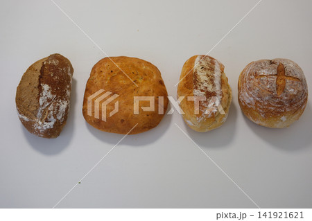 Four varieties of freshly baked bread on white table including round oval long and dark artisan loaves Four varieties of freshly baked bread on white table including round oval long and dark artisan loaves 141921621
