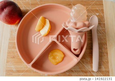 Aesthetic infant feeding accessories set with fruit puree and teether nibbler on a wood surface. Perfect stock photo for eco-friendly baby products, child nutrition, and parenting blogs Aesthetic infant feeding accessories set with fruit puree and teether nibbler on a wood surface. Perfect stock photo for eco-friendly baby products, child nutrition, and parenting blogs 141922131