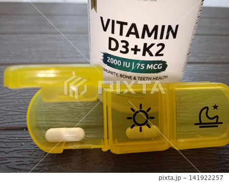 A medication organizer with vitamin D capsule in front of a supplement jar 141922257