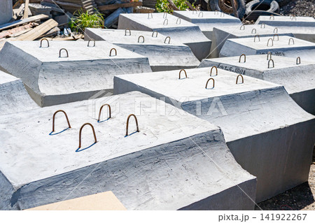 Large reinforced concrete foundation blocks lying on the ground ready for installation. Perfect stock photo for heavy construction, urban development, infrastructure, and material supply Large reinforced concrete foundation blocks lying on the ground ready for installation. Perfect stock photo for heavy construction, urban development, infrastructure, and material supply 141922267