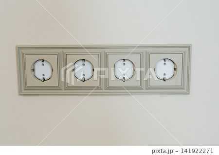 Horizontal frame with four European ground electric power outlets mounted on a beige wall. Perfect for electrical installation, home automation, power supply, and interior repair stock Horizontal frame with four European ground electric power outlets mounted on a beige wall. Perfect for electrical installation, home automation, power supply, and interior repair stock 141922271