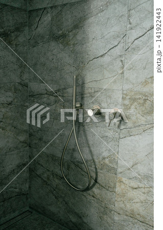 Chrome hand shower set with wall outlet and minimalist tap mixer inside a dark stone tiled walk-in shower. Perfect image for luxury bathroom renovation, sanitaryware, and spa design Chrome hand shower set with wall outlet and minimalist tap mixer inside a dark stone tiled walk-in shower. Perfect image for luxury bathroom renovation, sanitaryware, and spa design 141922443