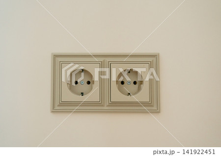 Beige double wall outlet with European grounding sockets in an ornate frame. Perfect stock photo for home electricity, classical room renovation, wall hardware, and electrical installation 141922451