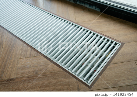 Sleek metal trench radiator in herringbone wood floor providing invisible thermal barrier near glass doors. Great image for heating system design, smart homes, and modern living spaces 141922454