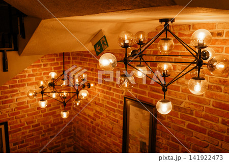 Stylish geometric pendant lights glowing above a wooden staircase with brick wall. Perfect stock image for modern cafe interiors, industrial style lighting, atmosphere, and home renovation Stylish geometric pendant lights glowing above a wooden staircase with brick wall. Perfect stock image for modern cafe interiors, industrial style lighting, atmosphere, and home renovation 141922473