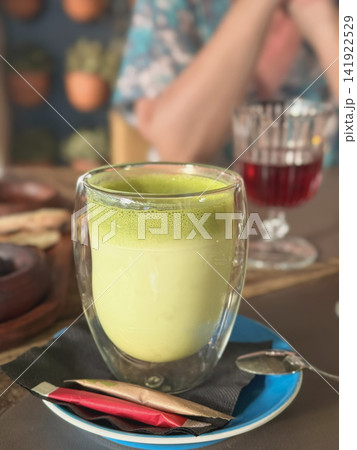 Matcha Latte in Double Wall Glass. Creamy green matcha latte served in transparent double wall glass at cafe table. Modern drink scene, wellness, tea culture, healthy lifestyle, relaxing coffee shop Matcha Latte in Double Wall Glass. Creamy green matcha latte served in transparent double wall glass at cafe table. Modern drink scene, wellness, tea culture, healthy lifestyle, relaxing coffee shop 141922529
