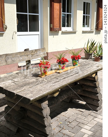 A large log table and a bench with pots of red flowers on the house's summer terrace. 141924324