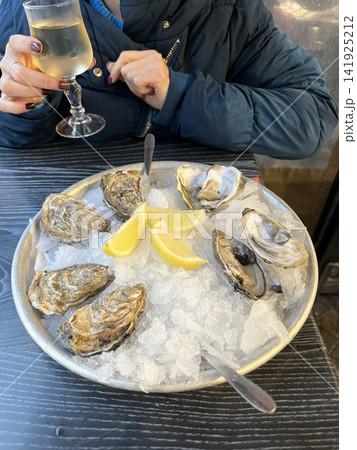 Fresh Oysters on Ice with Lemon Wedges and Glass of White Wine in Restaurant 141925212