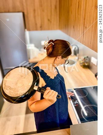 Woman Holding Frying Pan While Turning on Electric Stove Top in Modern Kitchen 141925213