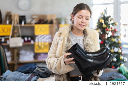 Positive young woman choosing platform boots in clothing store Positive young woman choosing platform boots in clothing store 141925737