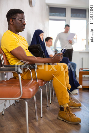 Adult african man waiting in line with phone in his hand Adult african man waiting in line with phone in his hand 141925845