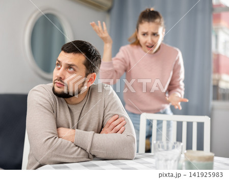 Upset guy sitting at table with frustrated girlfriend in background 141925983