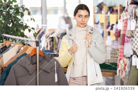 Young Armenian woman is fitting on and trying on down jacket in store 141926339