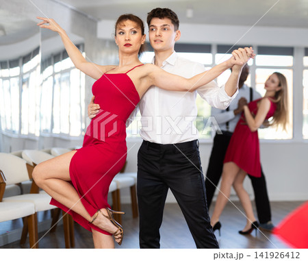 Happy young man and woman in elegant clothes performing ballroom dance in dancing room during celebration or party Happy young man and woman in elegant clothes performing ballroom dance in dancing room during celebration or party 141926412