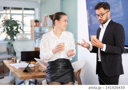 Man and a woman work in an office, they stand near a table and drink coffee 141926430