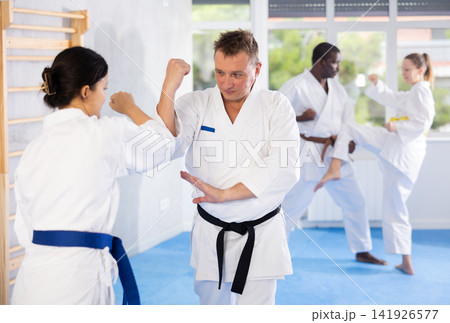 Middle-aged man attendee of karate classes fighting with his opponent in sports hall Middle-aged man attendee of karate classes fighting with his opponent in sports hall 141926577