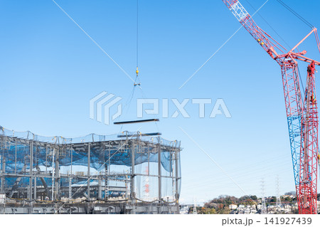 タワークレーンで鉄骨造の建物へ建築資材を吊り上げる建設現場1 タワークレーンで鉄骨造の建物へ建築資材を吊り上げる建設現場1 141927439
