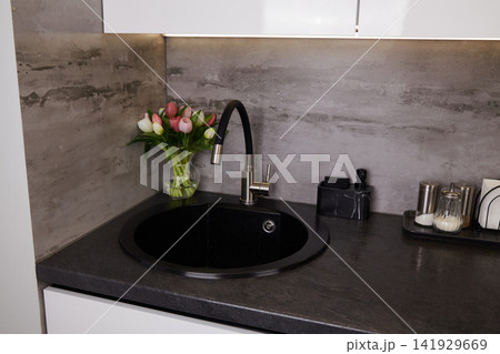 Modern kitchen sink area with flowers, utensils, and a clean countertop space for cooking and meal preparation Modern kitchen sink area with flowers, utensils, and a clean countertop space for cooking and meal preparation 141929669