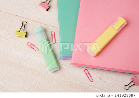 Colorful school supplies are laid out on a wooden table. There are two notebooks here, one pink and one green  141929697
