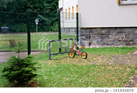 Children balance bike parked in a metal rack on green grass lawn near a building Children balance bike parked in a metal rack on green grass lawn near a building 141930859
