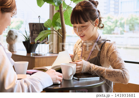カフェで手帳を見ながら会話を楽しむ女性二人 カフェで手帳を見ながら会話を楽しむ女性二人 141931681